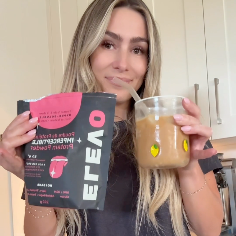 Woman holding a package of ELEVO Nutrition powder and a glass of iced coffee.