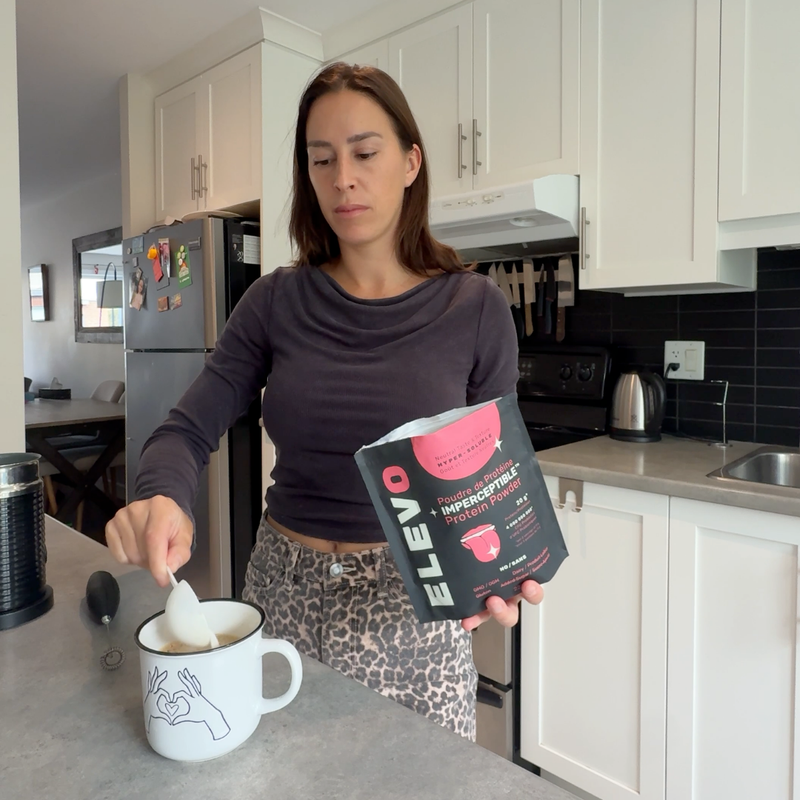 Woman in a kitchen holding a bag of Elevo Nutrition protein powder and a mug.
