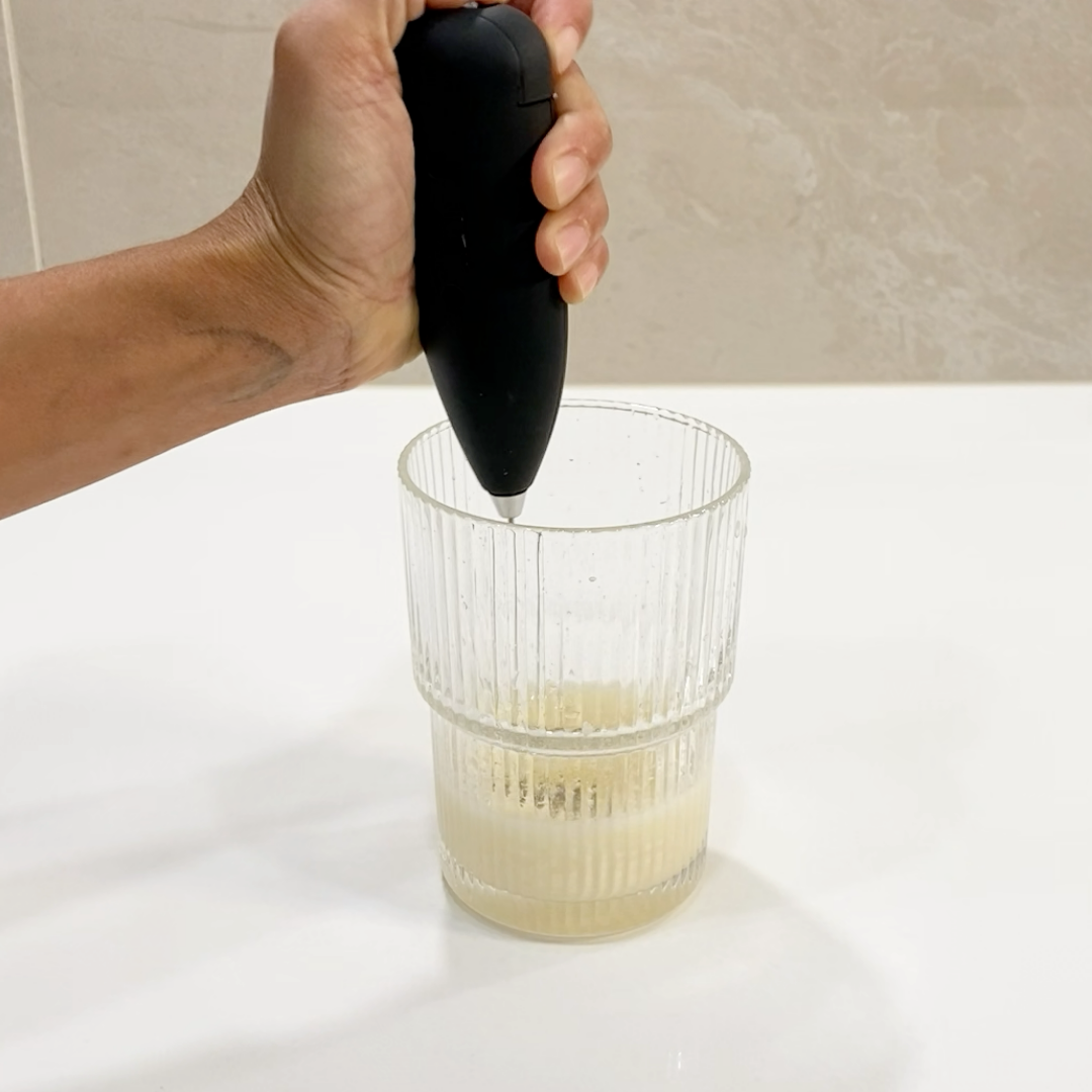 Hand using a black handheld device to extract juice from a glass of fruit