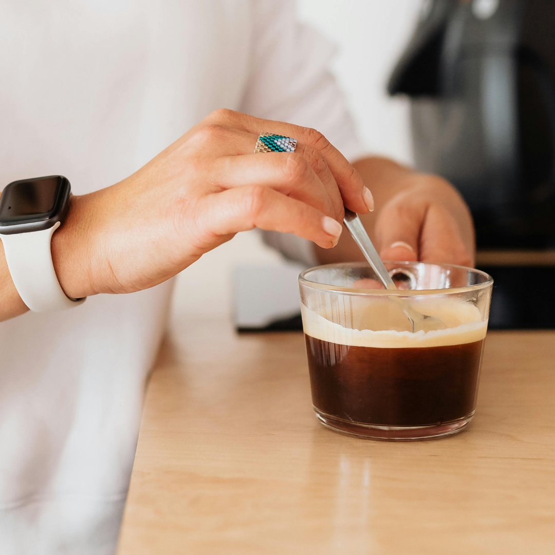 Person stirring a glass of coffee with a spoon after pouring your favorite protein powder