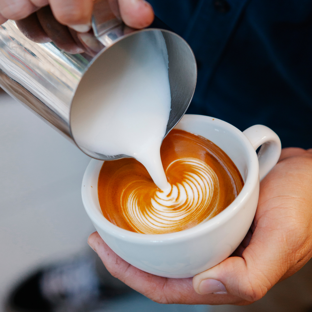 Person pouring milk into a cup of coffee to create latte art.