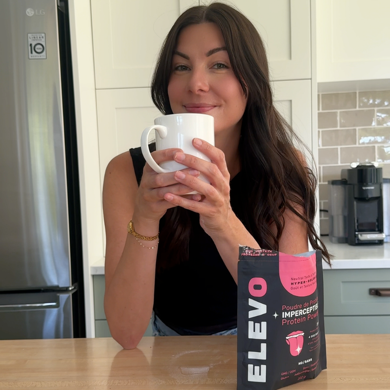 Woman holding a mug in a kitchen with an ELEVO Nutrition protein powder package on the counter.